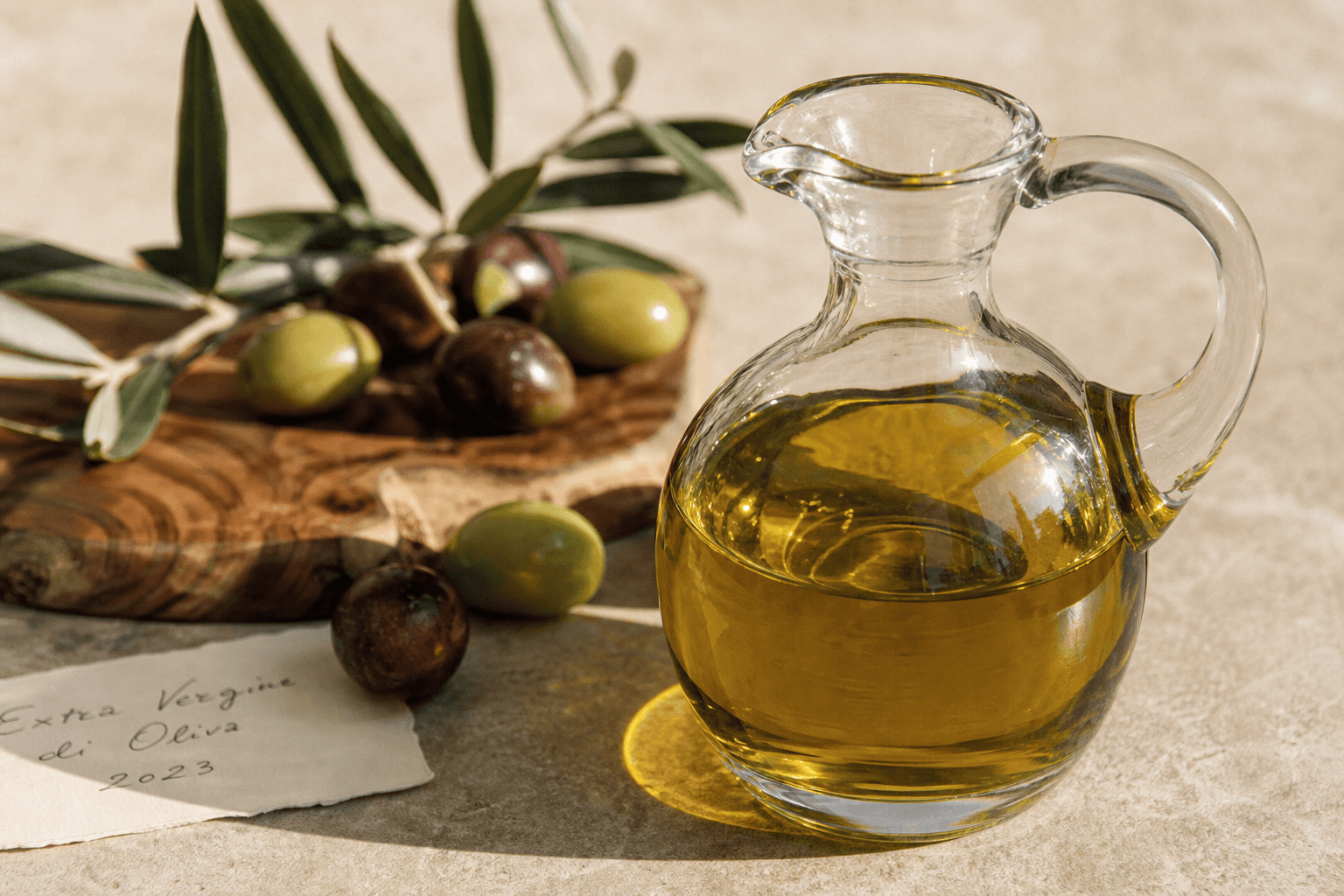 Premium olive oil in a glass cruet beside ripe olives and olive leaves on weathered wood